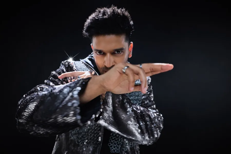 Guru Randhawa in a silver sequin jacket, hands crossed in front of his face