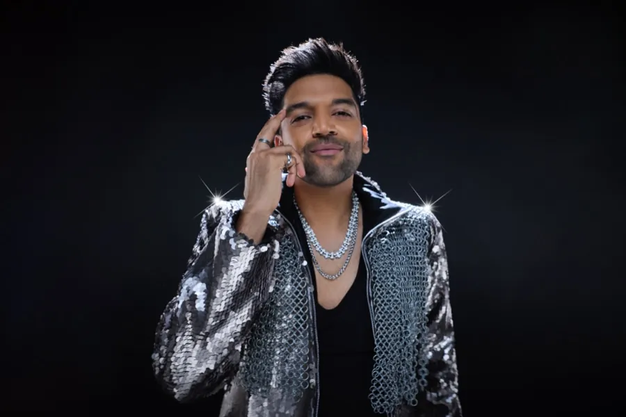 Guru Randhawa smiling, hand at his ear